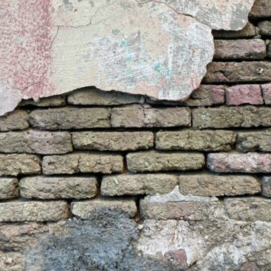 A wall with crumbling plaster and exposed brick